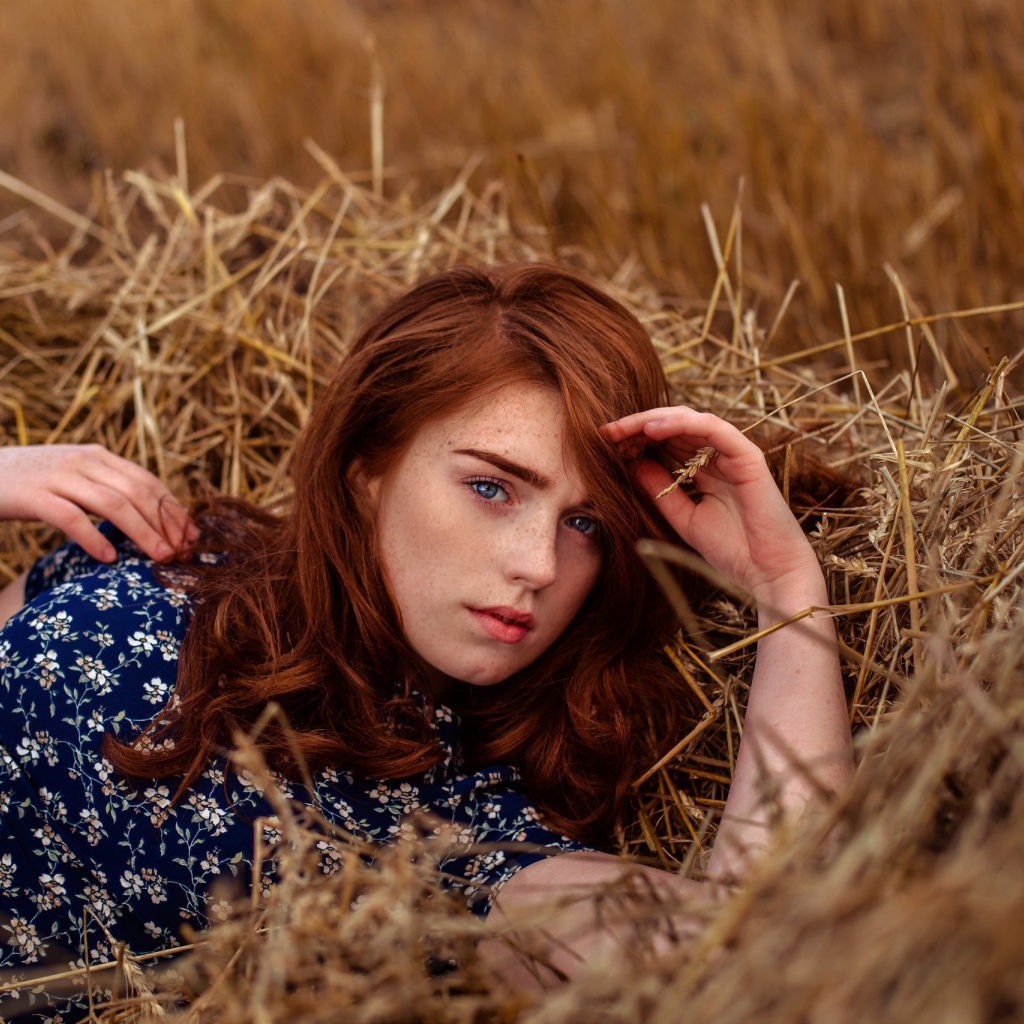 Красивая голубоглазая рыжеволосая девушка лежит в сене