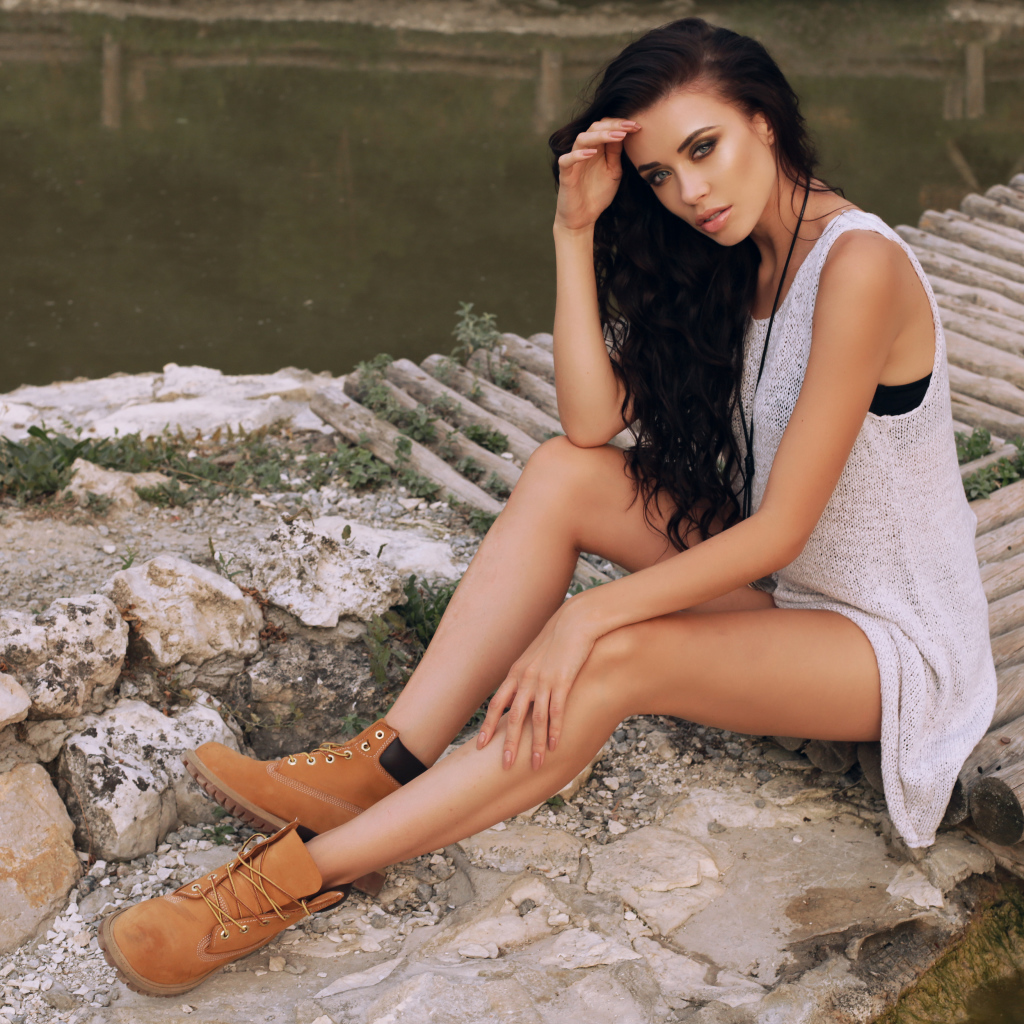 Красивая девушка брюнетка сидит у воды на мостике