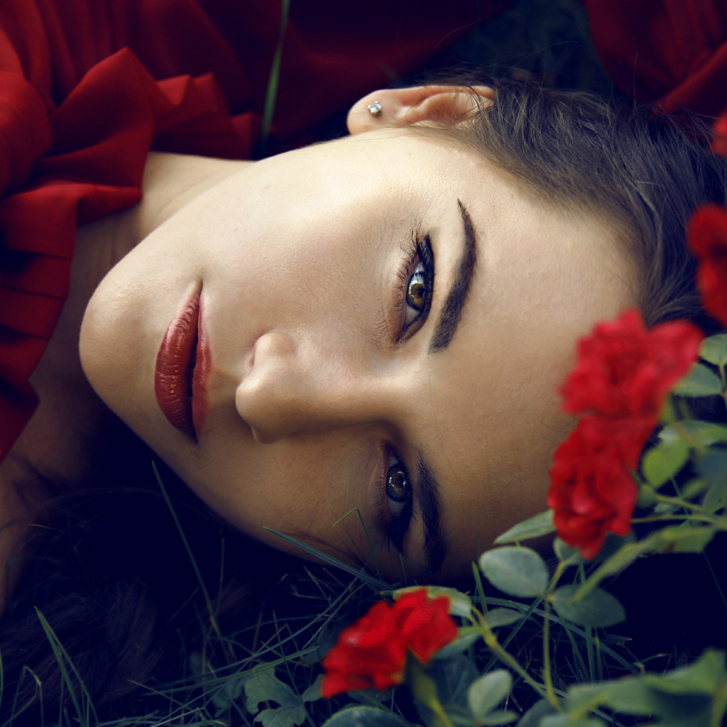 Красивая брюнетка лежит на траве с красными розами