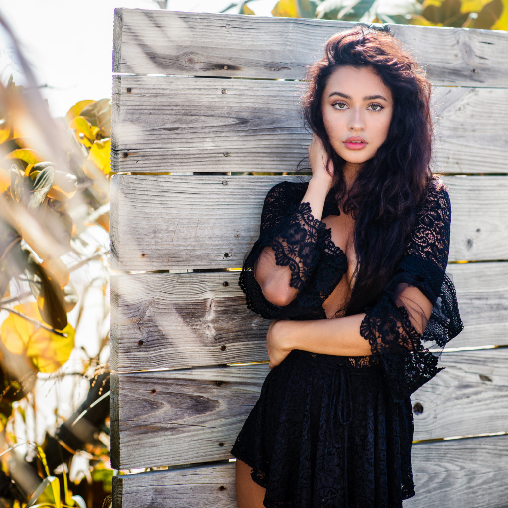 Красивая девушка в черном платье у стены 