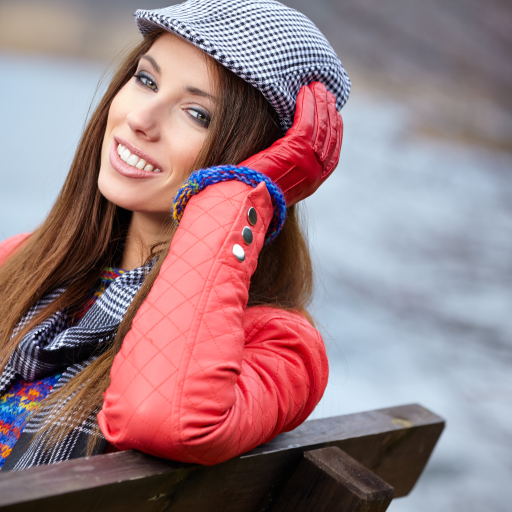 Красивая девушка в красной куртке сидит на лавке