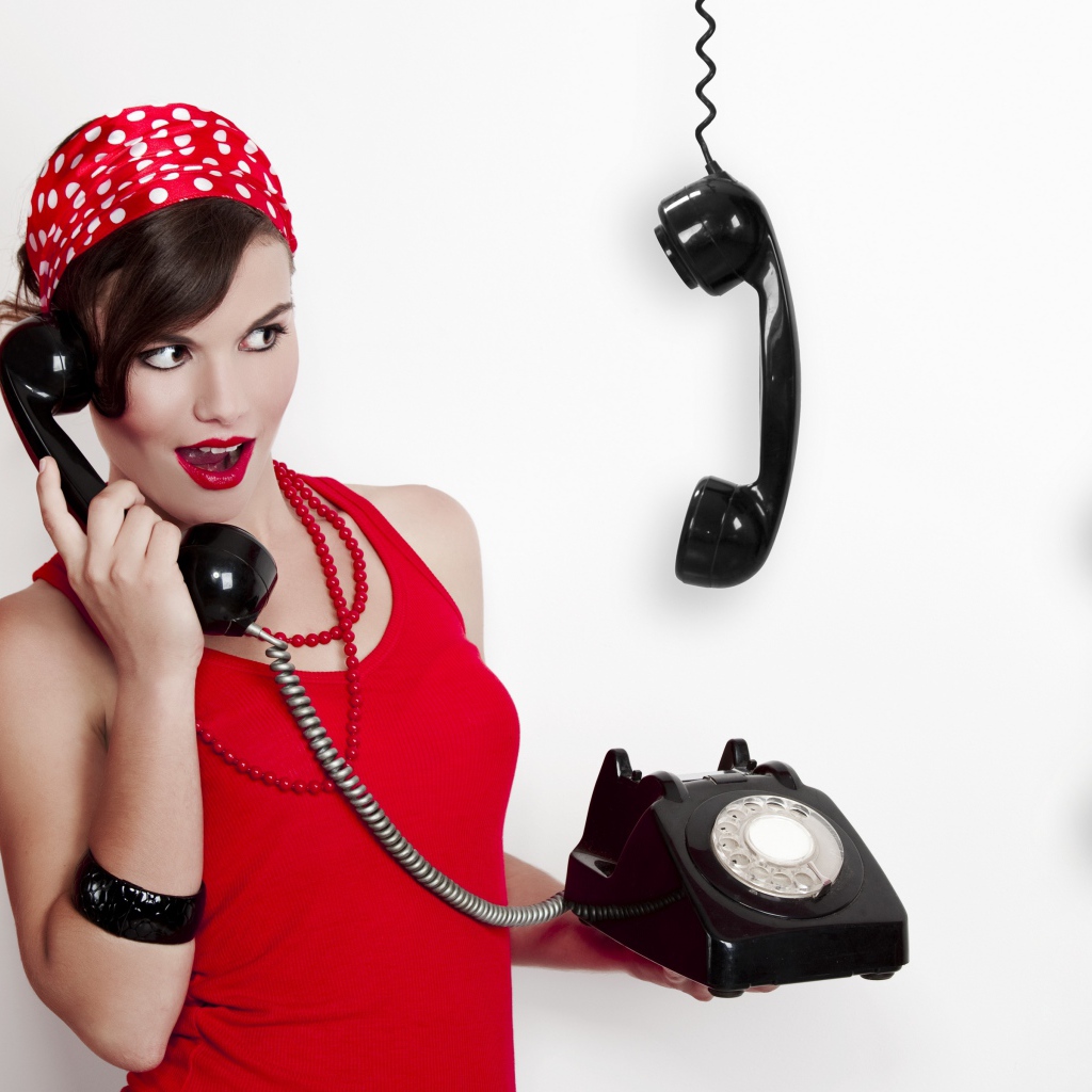 Красивая девушка в красном с черным старым телефоном в руках