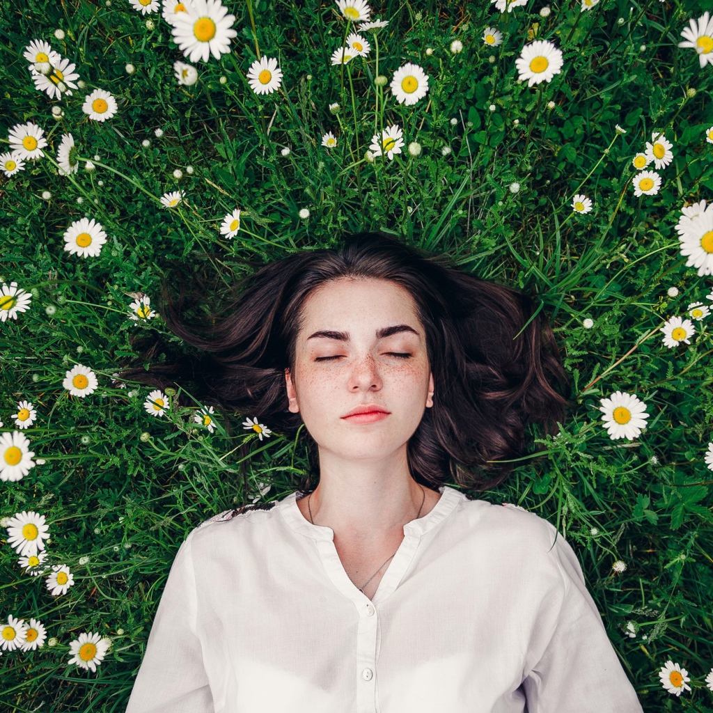 Красивая девушка лежит на зеленой траве с ромашками