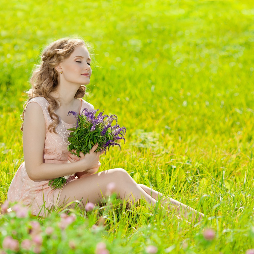 Красивая девушка с букетом сидит на зеленой траве