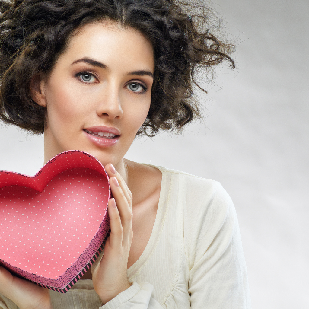 Красивая девушка с коробкой в форме сердца в руках на сером фоне