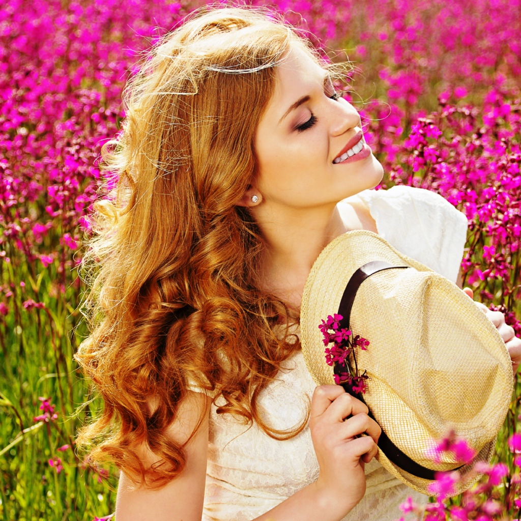 Красивая девушка с шляпой в руках на поле с розовыми цветами