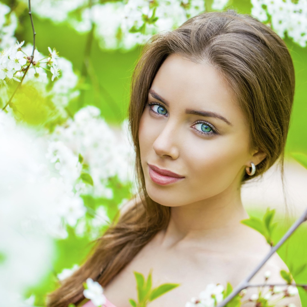 Красивая зеленоглазая девушка у цветущей вишни 