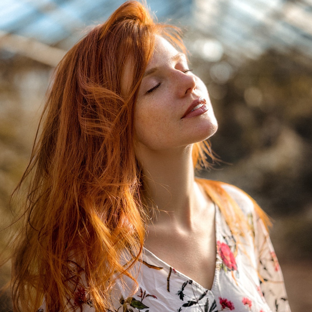 Красивая рыжеволосая девушка нежится в лучах солнца