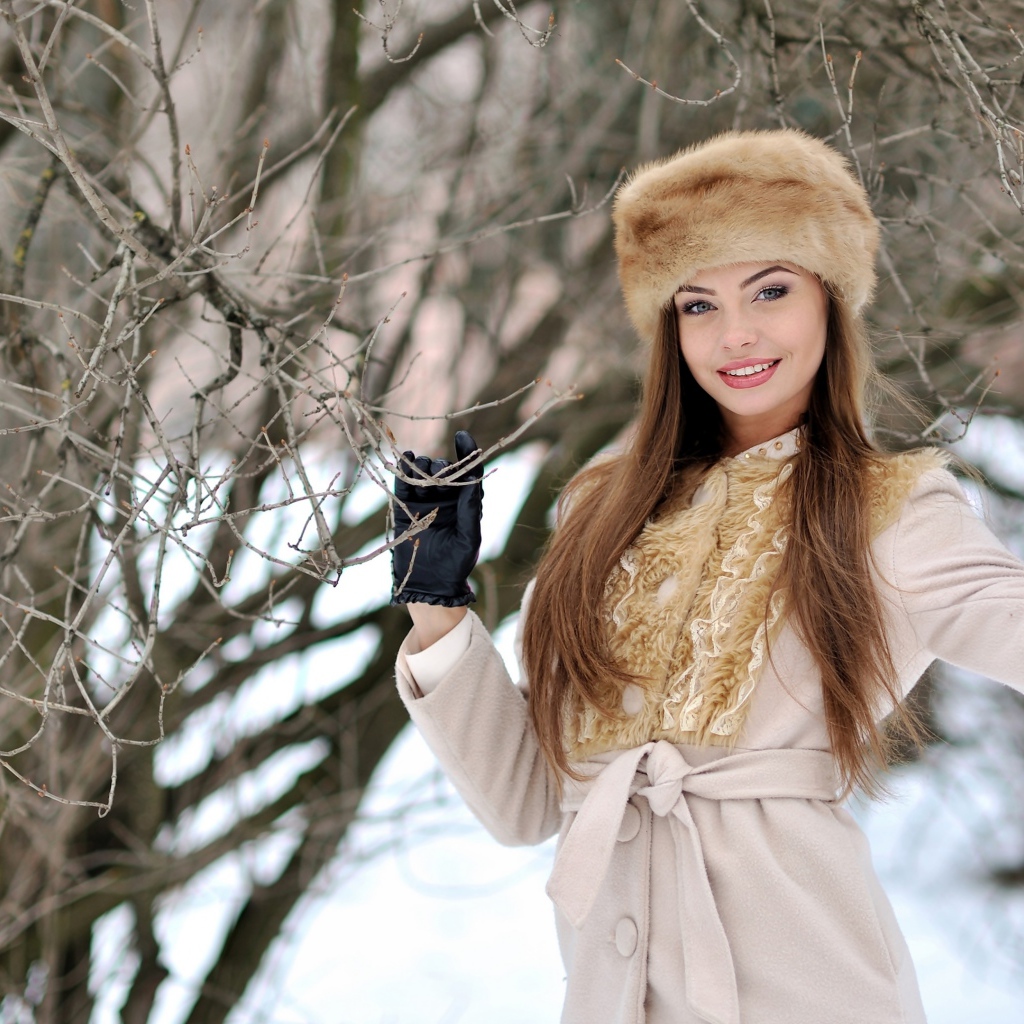 Красивая улыбающаяся девушка в шапке у дерева зимой