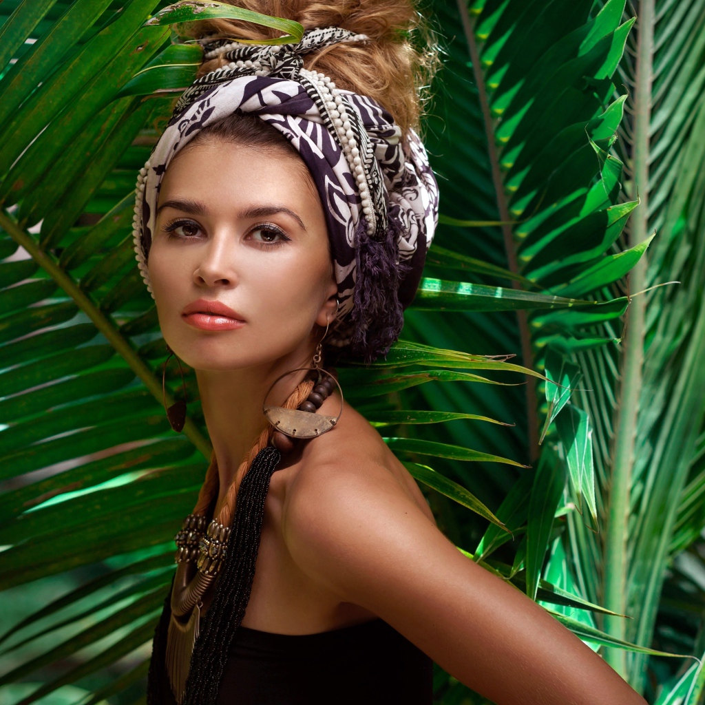 Красивая женщина в тюрбане с украшениями среди зеленых пальмовых листьев