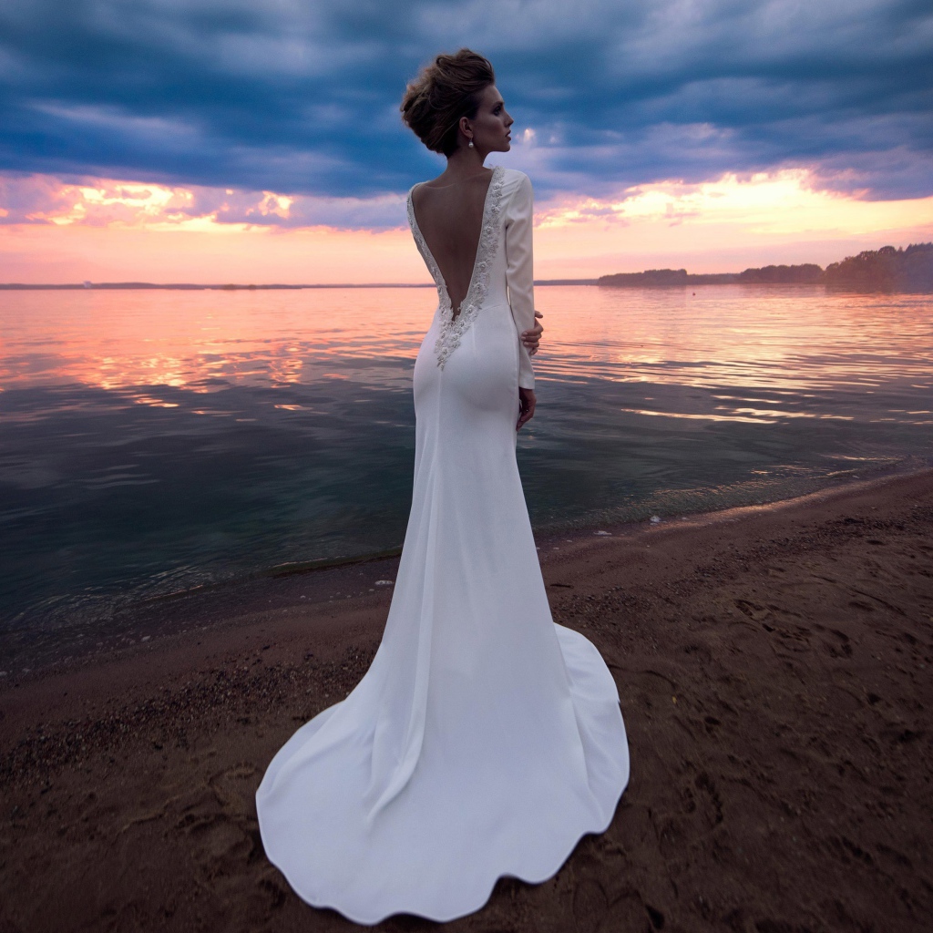 Красивая молодая девушка в свадебном платье у воды на закате 