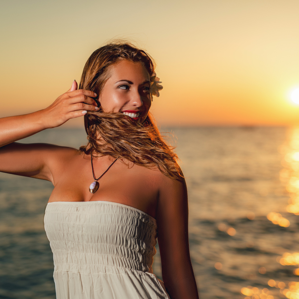 Очаровательная улыбающаяся девушка шатенка на берегу моря на закате