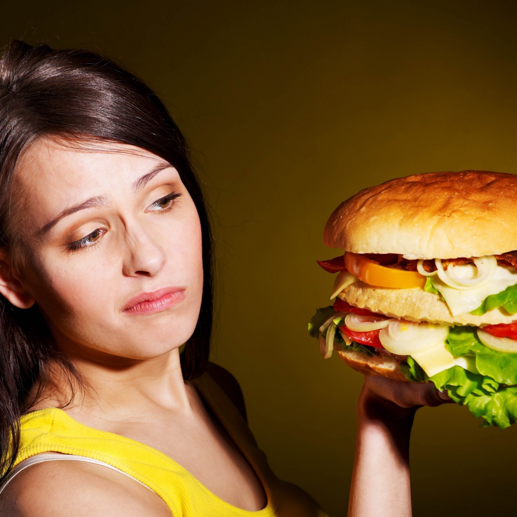Недовольная девушка с большим гамбургером в руках 