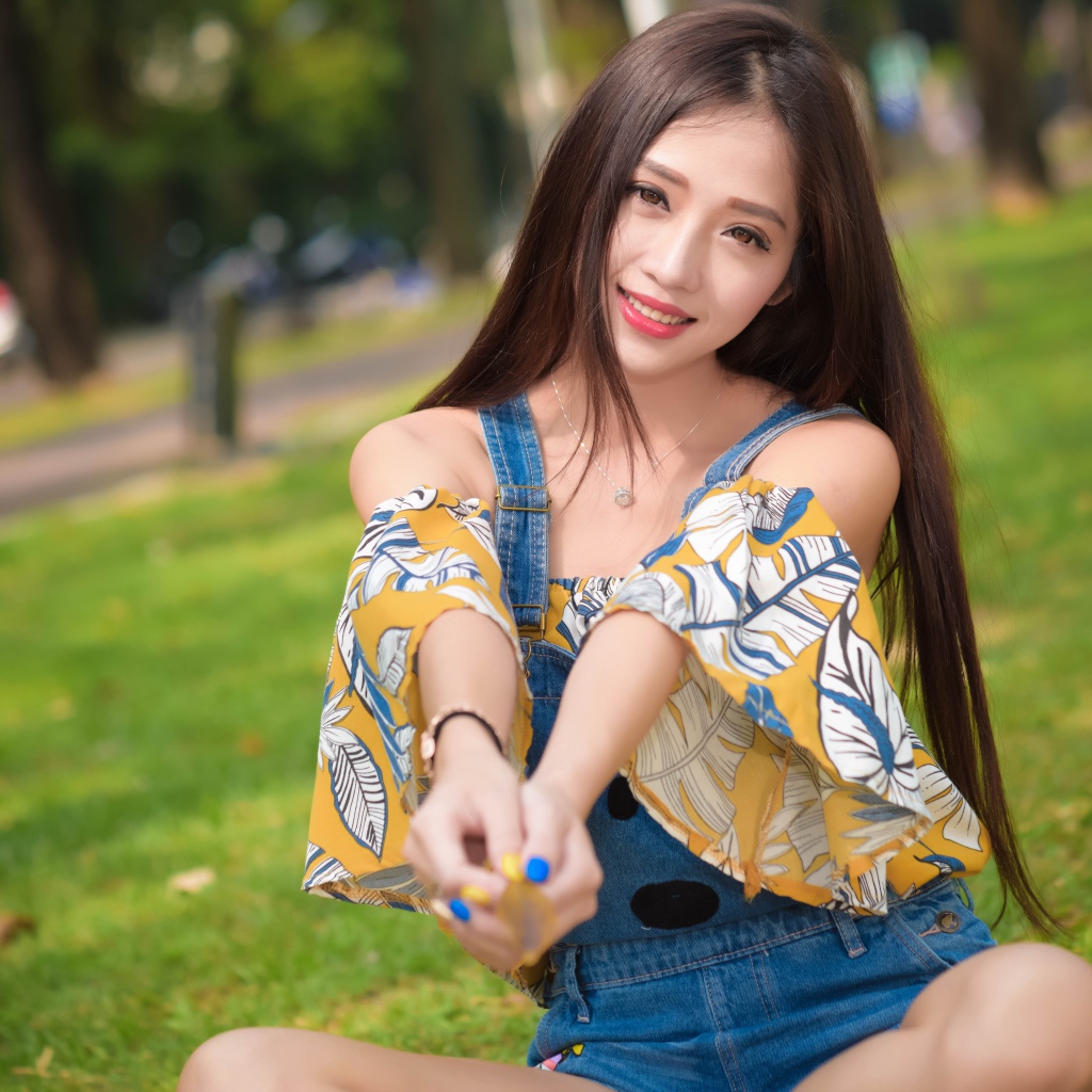 Улыбающаяся девушка азиатка сидит на траве