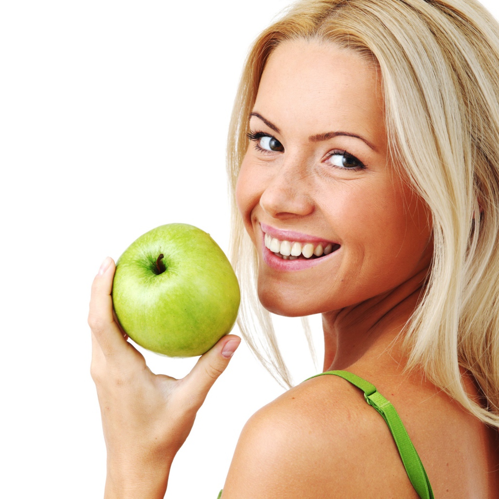Улыбающаяся девушка блондинка с зеленым яблоком в руке на белом фоне