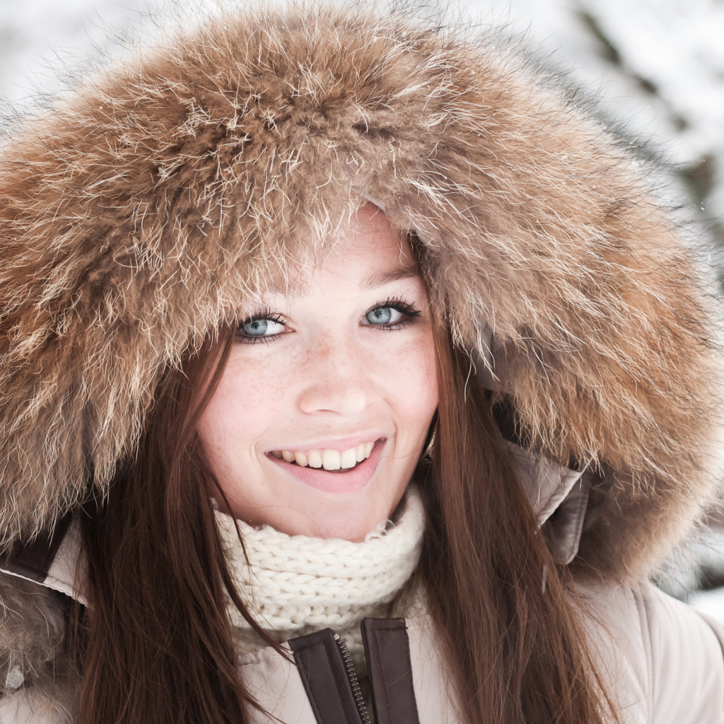 Улыбающаяся голубоглазая девушка в капюшоне зимой