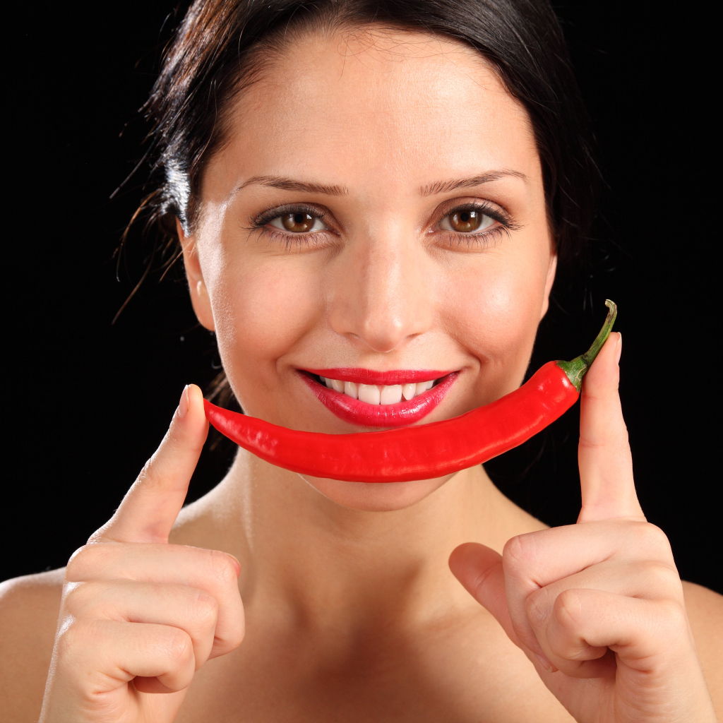 Улыбающаяся девушка с красным перцем на черном фоне