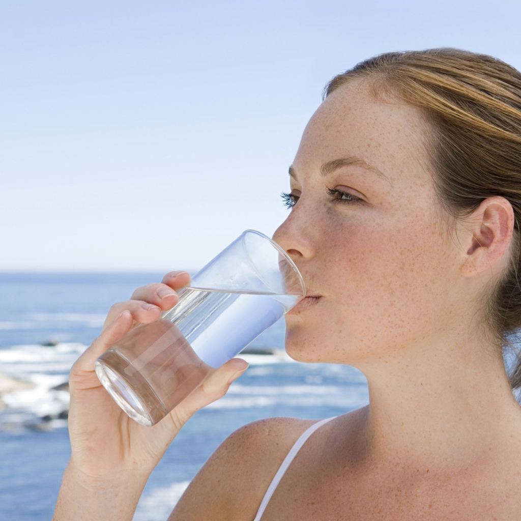 Девушка пьет воду со стакана на фоне моря