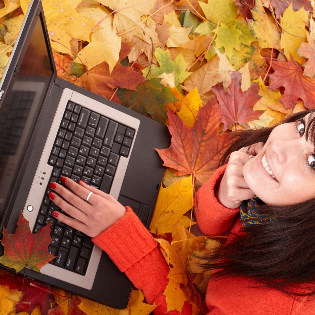 Девушка лежит на сухой опавшей листве с ноутбуком осенью