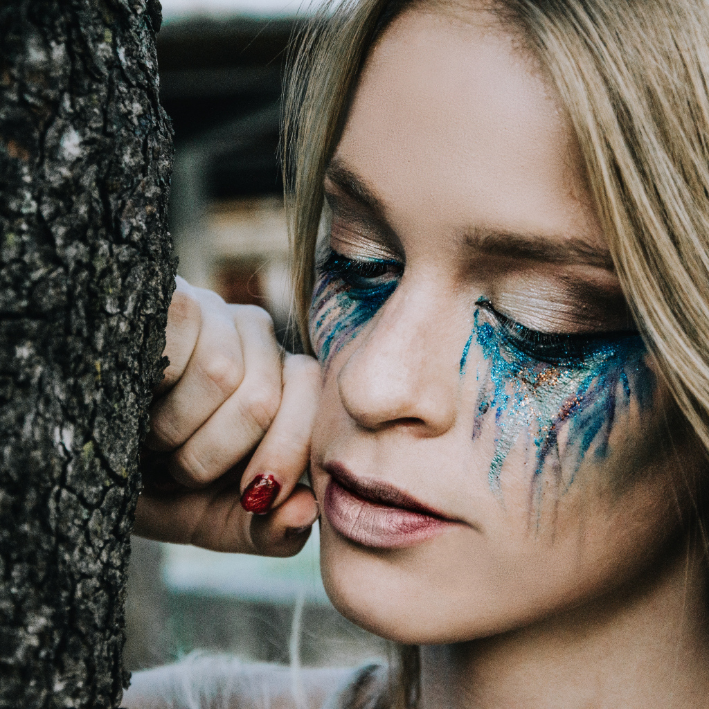 Заплаканная блондинка стоит у дерева