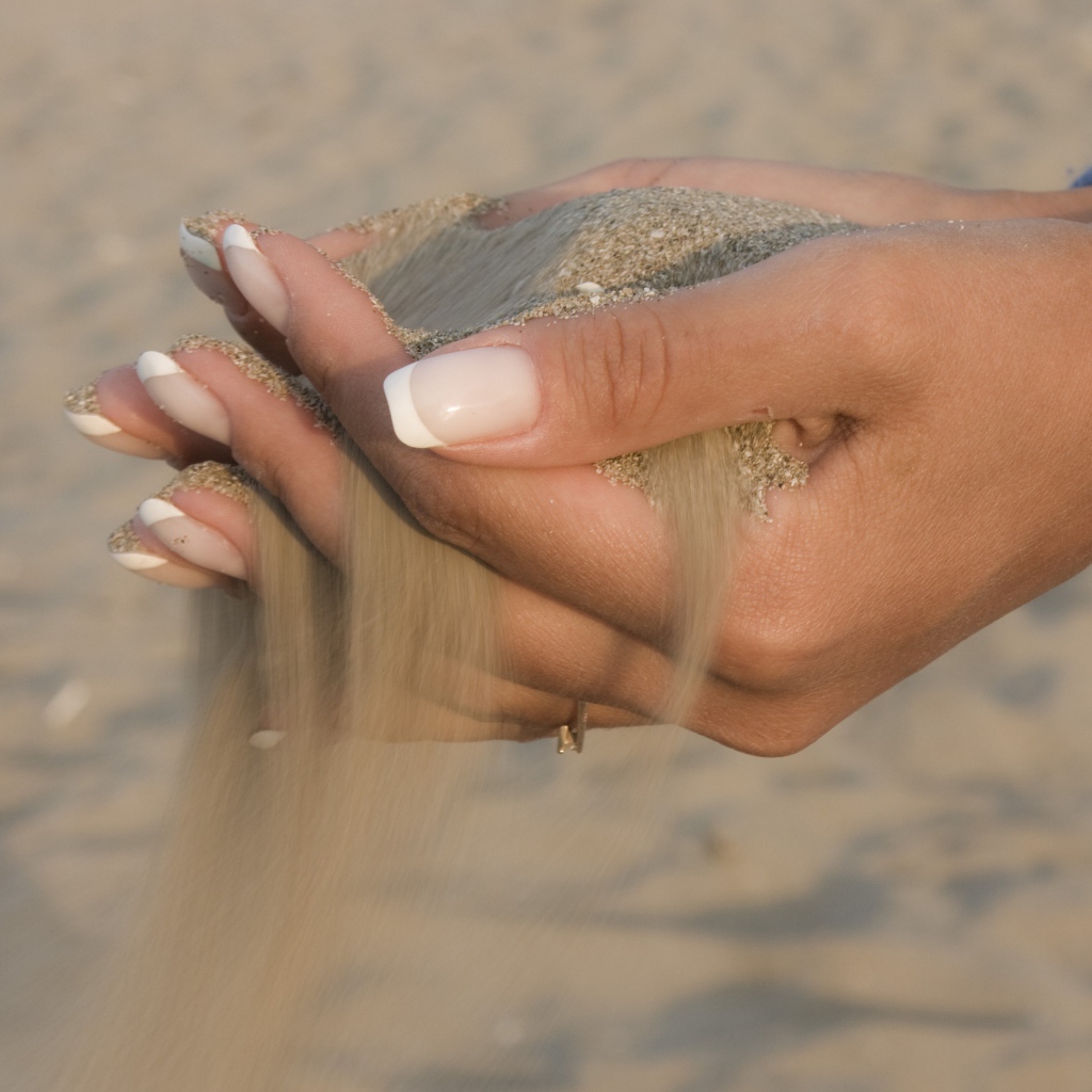 Желтый песок в руках у девушки с красивым маникюром