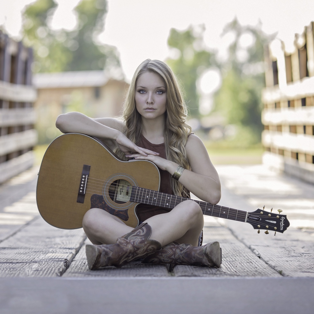 Молодая девушка блондинка сидит на мосту с гитарой
