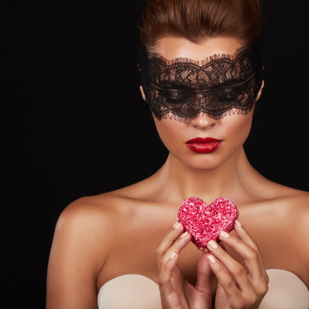 Молодая девушка в черной маске с красным сердцем в руках