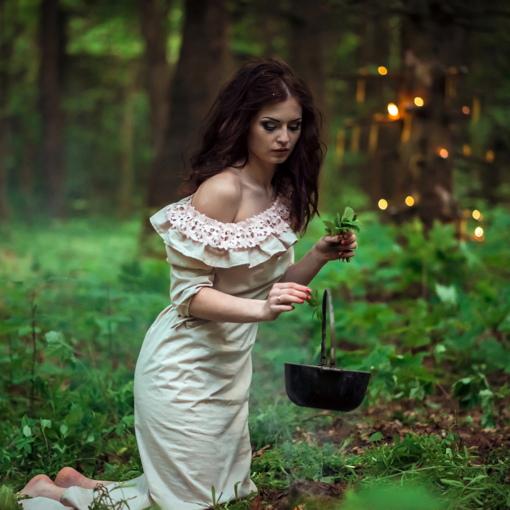 Молодая девушка колдунья варит зелье в лесу