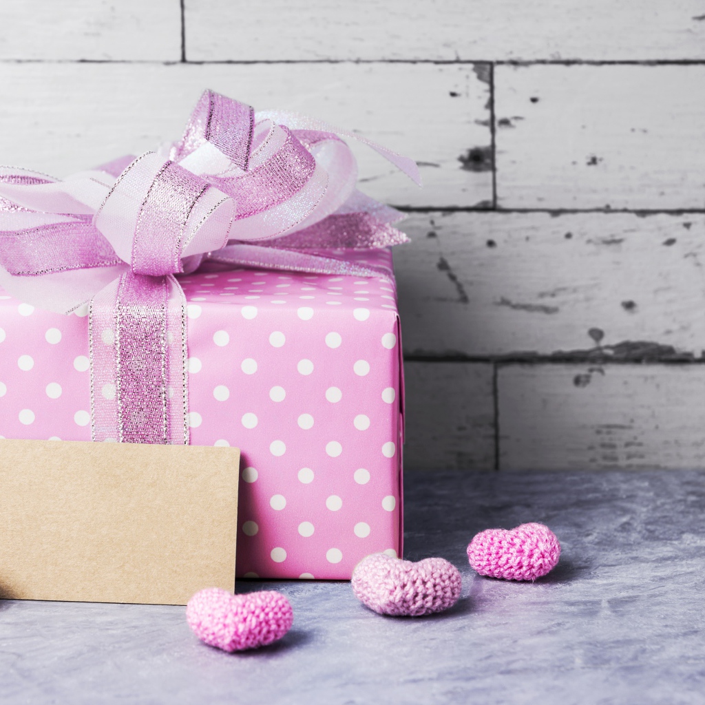 Большая сиреневая подарочная коробка с бантом и маленькими сердечками на фоне стены