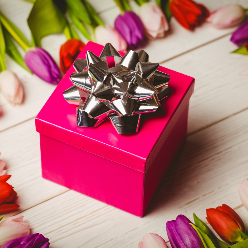 Красная коробка с подарком на столе с тюльпанами