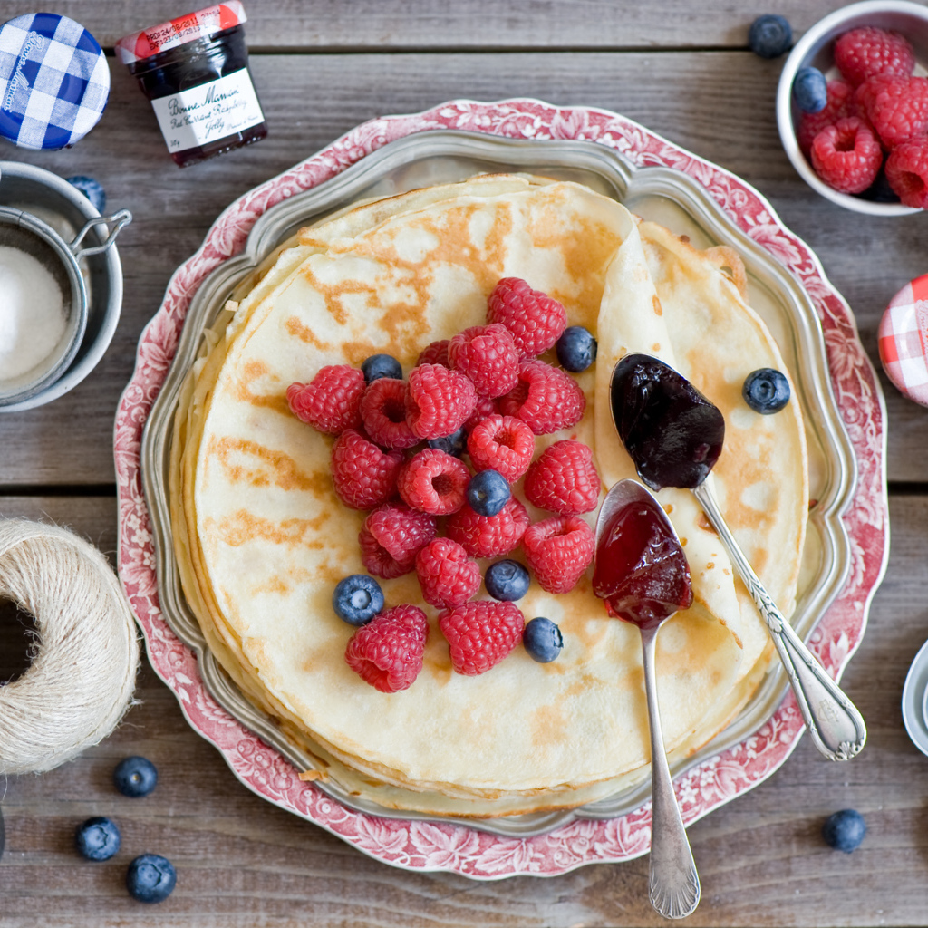Тонкие блины с малиной и черникой на столе вид сверху
