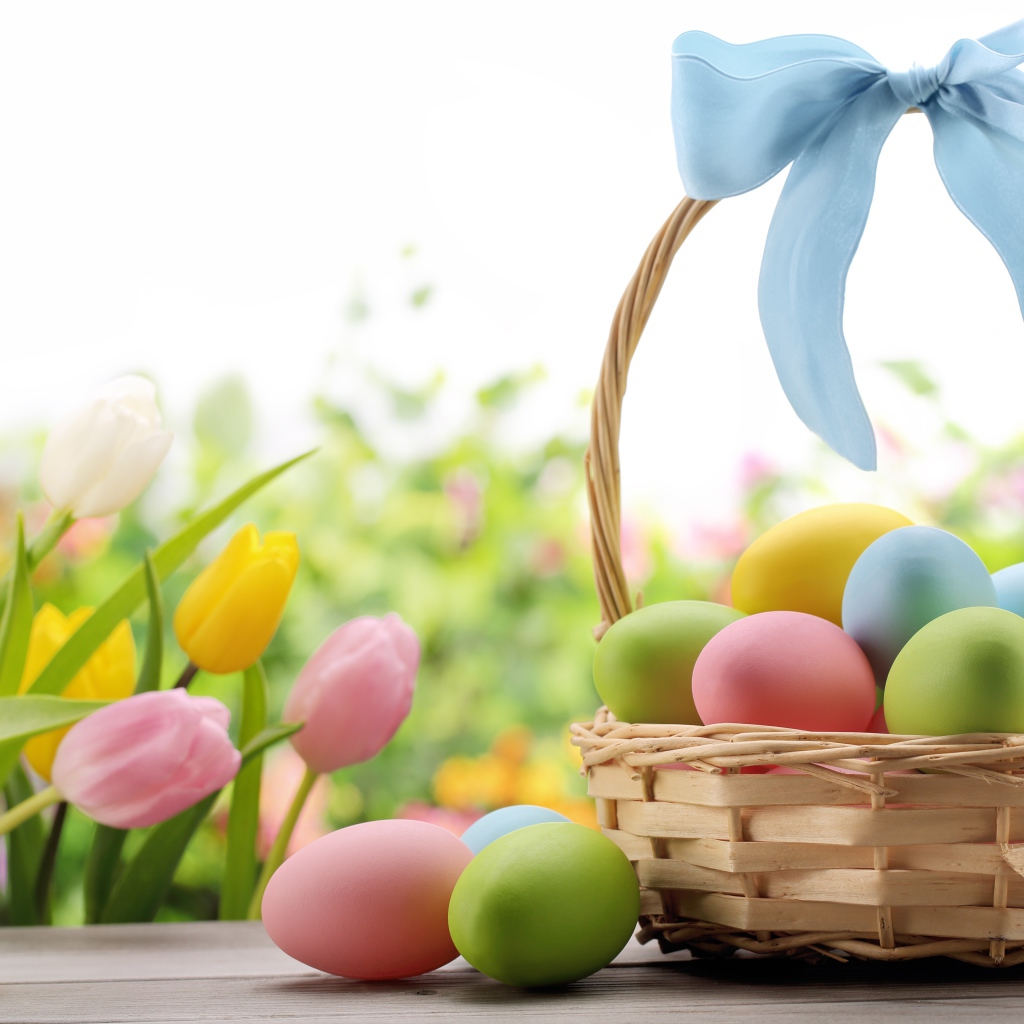 Корзина крашеных яиц с голубым бантом  на фоне тюльпанов на  Пасху