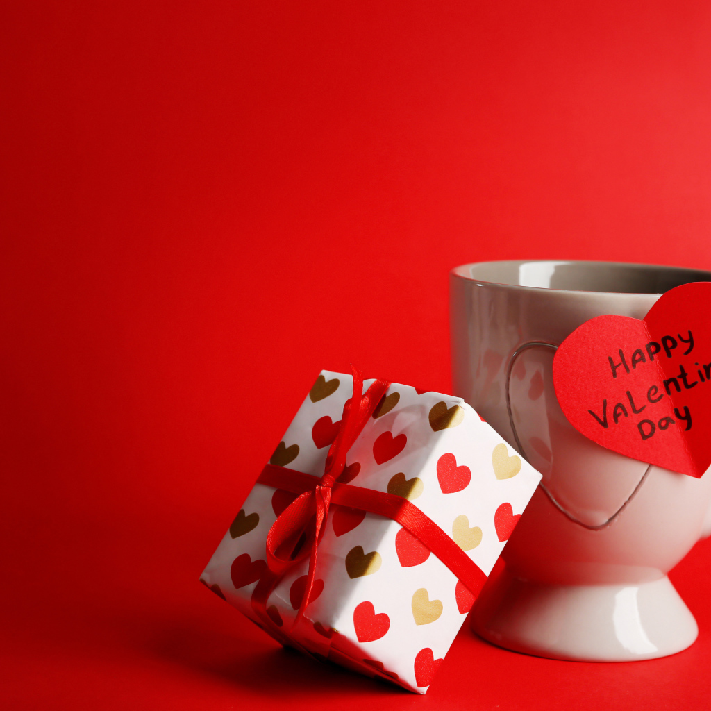 Чашка с подарком и валентинкой на красном фоне на 14 февраля