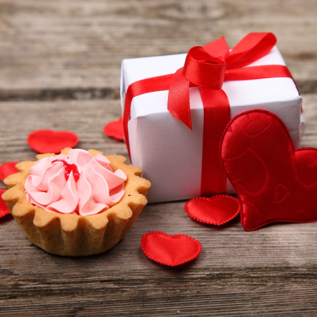 Пирожное, подарок и сердечки на деревянном фоне на День Святого Валентина