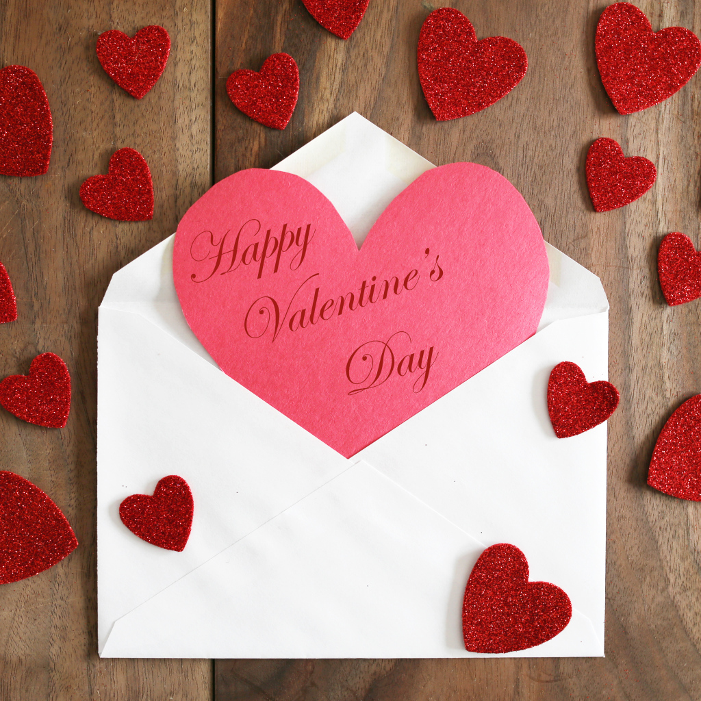 Белый конверт с валентинкой на деревянном столе с красными сердечками на 14 февраля