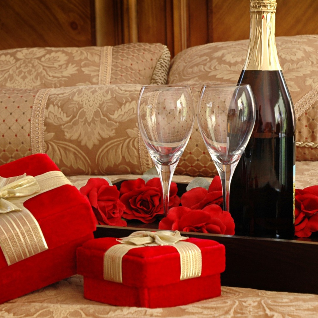Бутылка вина, два бокала и подарки для романтического вечера на кровати 