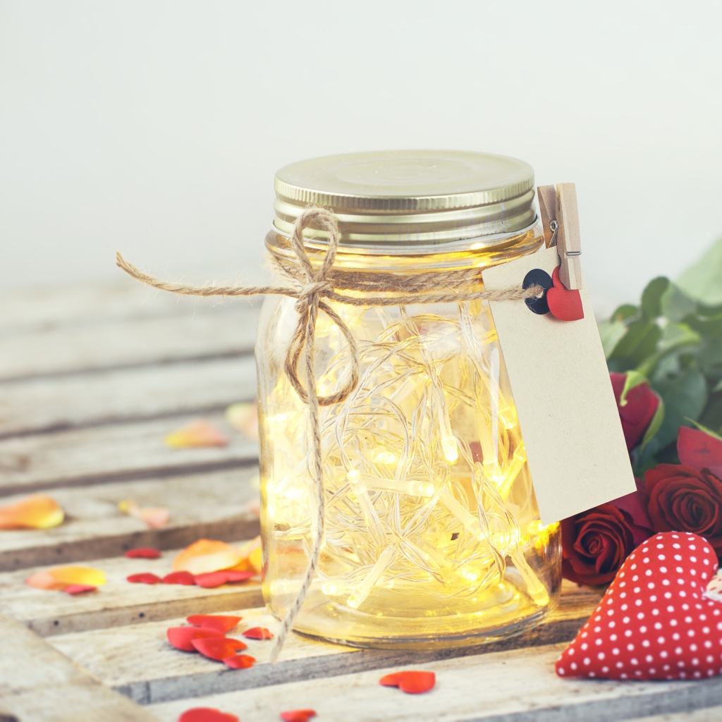 Стеклянная банка с гирляндой на столе с букетом роз и сердечками