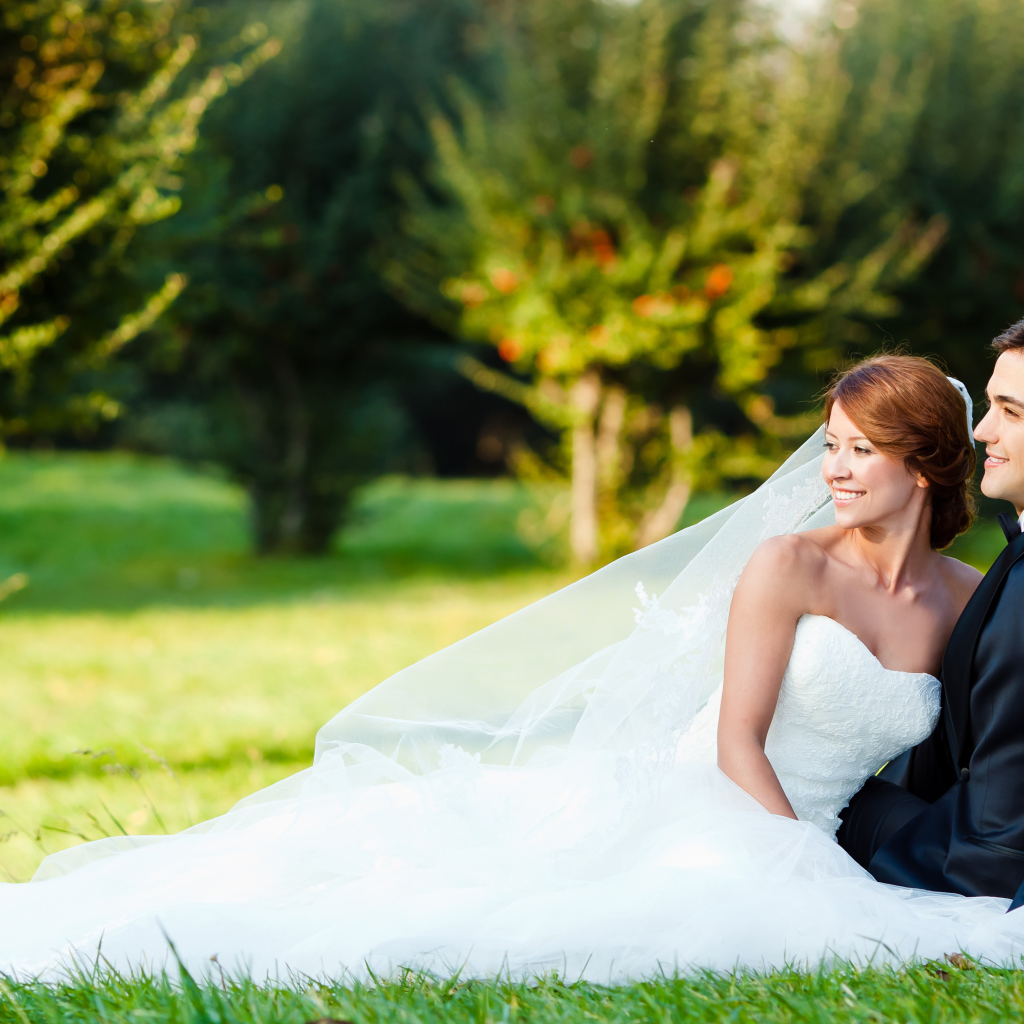 Счастливые жених и невеста сидят на зеленой траве