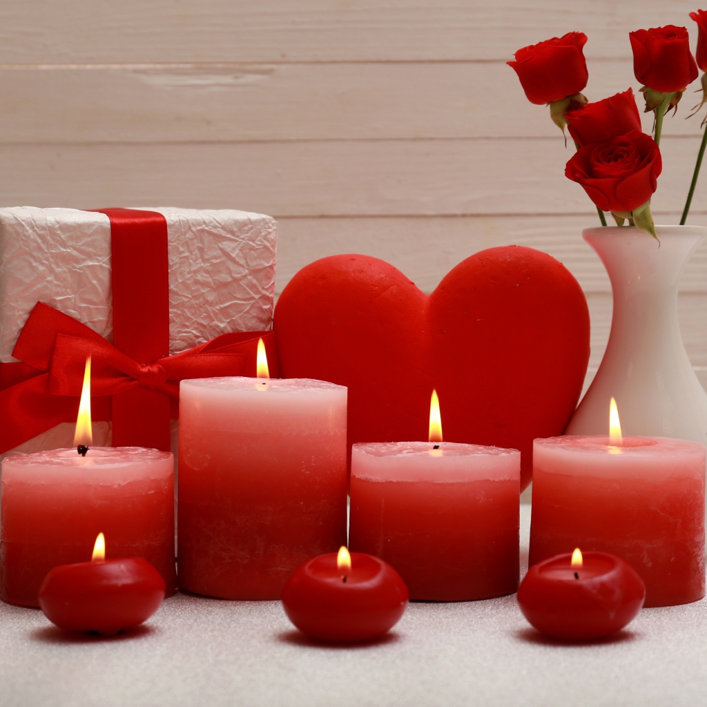 Зажженные красные свечи на столе с подарком, красным сердцем и цветами в вазе 