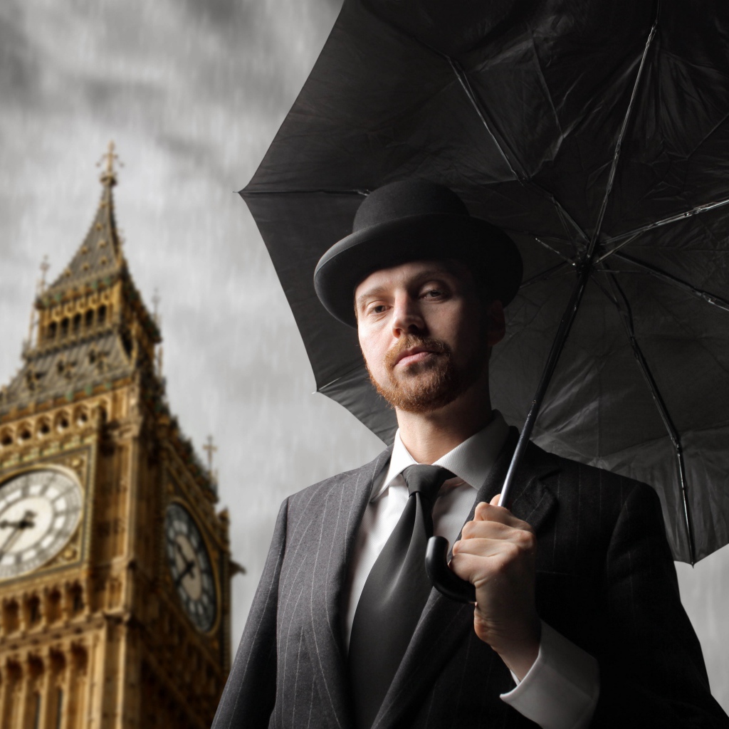 Мужчина в костюме с черным зонтом у башни с часами 