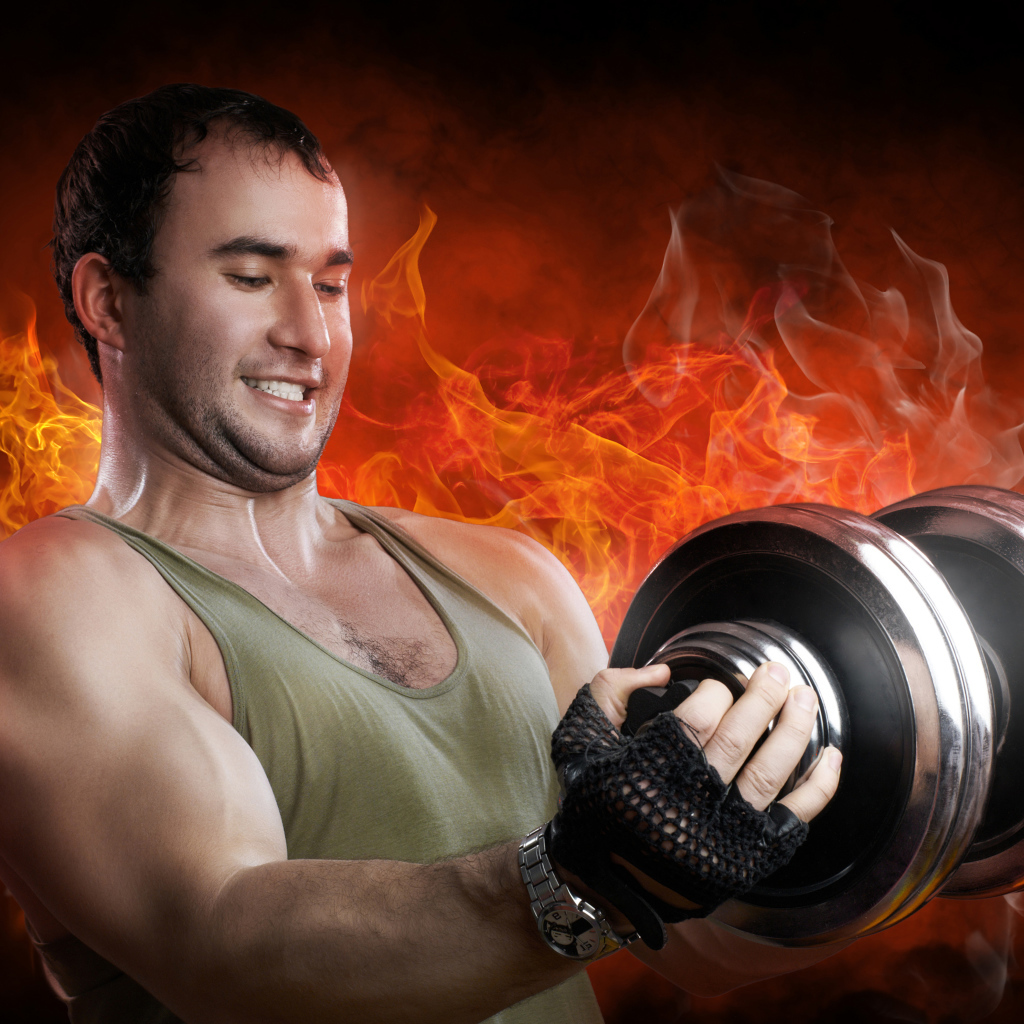 Мужчина спортсмен держит в руках гантелю на фоне огня