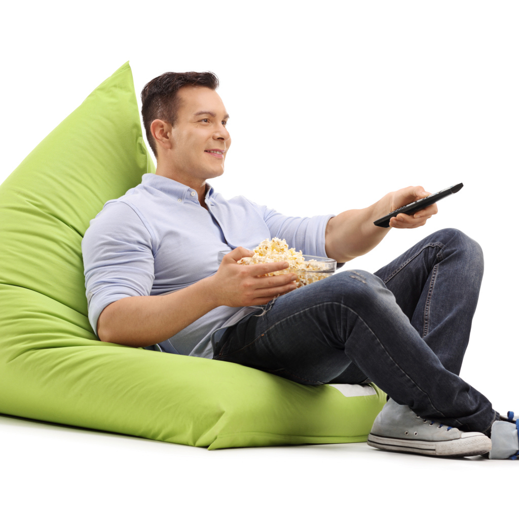 A man with popcorn and a TV remote is lying on a green pillow