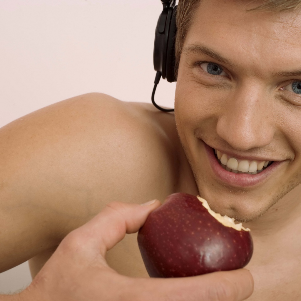 Красивый голубоглазый парень в наушниках с яблоком в руке