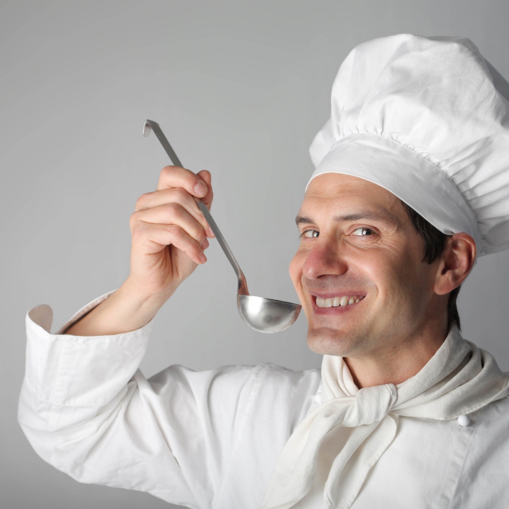 Улыбающийся мужчина повар с половником в руках на сером фоне