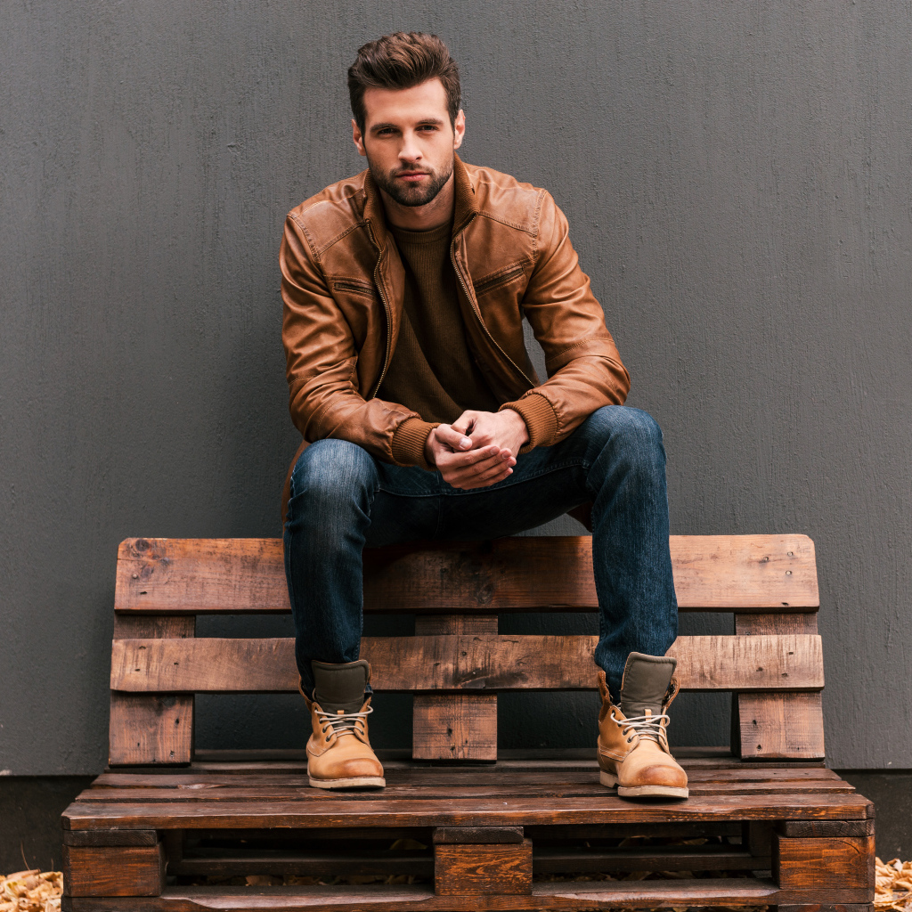 Молодой красивый мужчина сидит на деревянной лавке