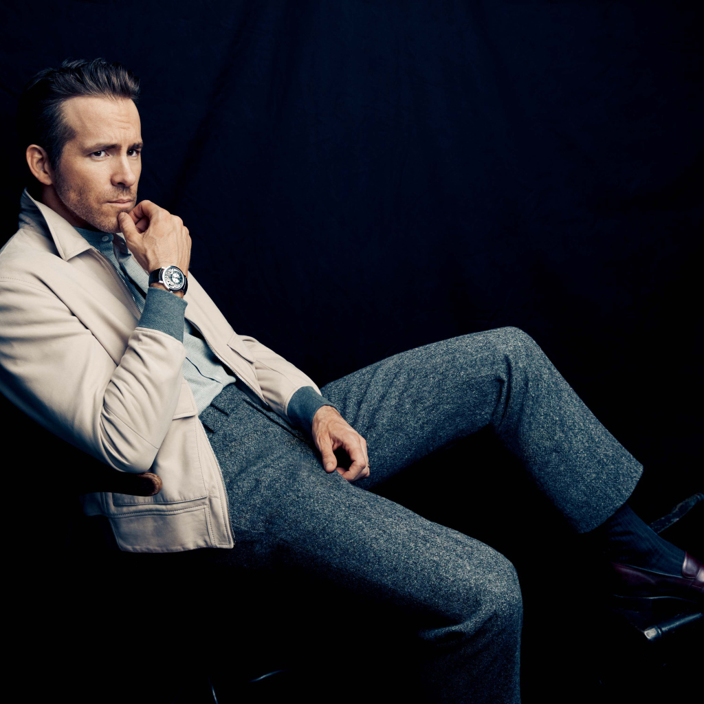 Actor Ryan Reynolds is sitting on a chair with a clock on his hand