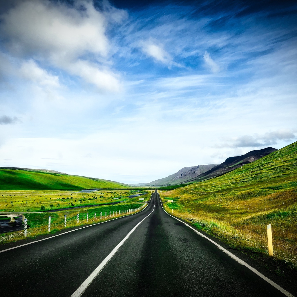 Ровная дорога у зеленых холмов на фоне голубого неба