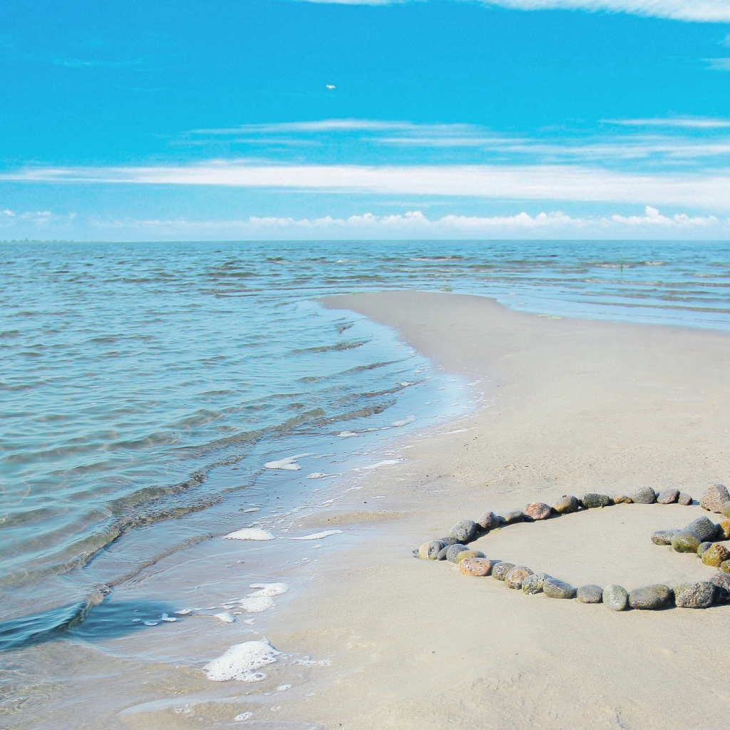 Сердце из камней на песке у спокойного моря под голубым небом