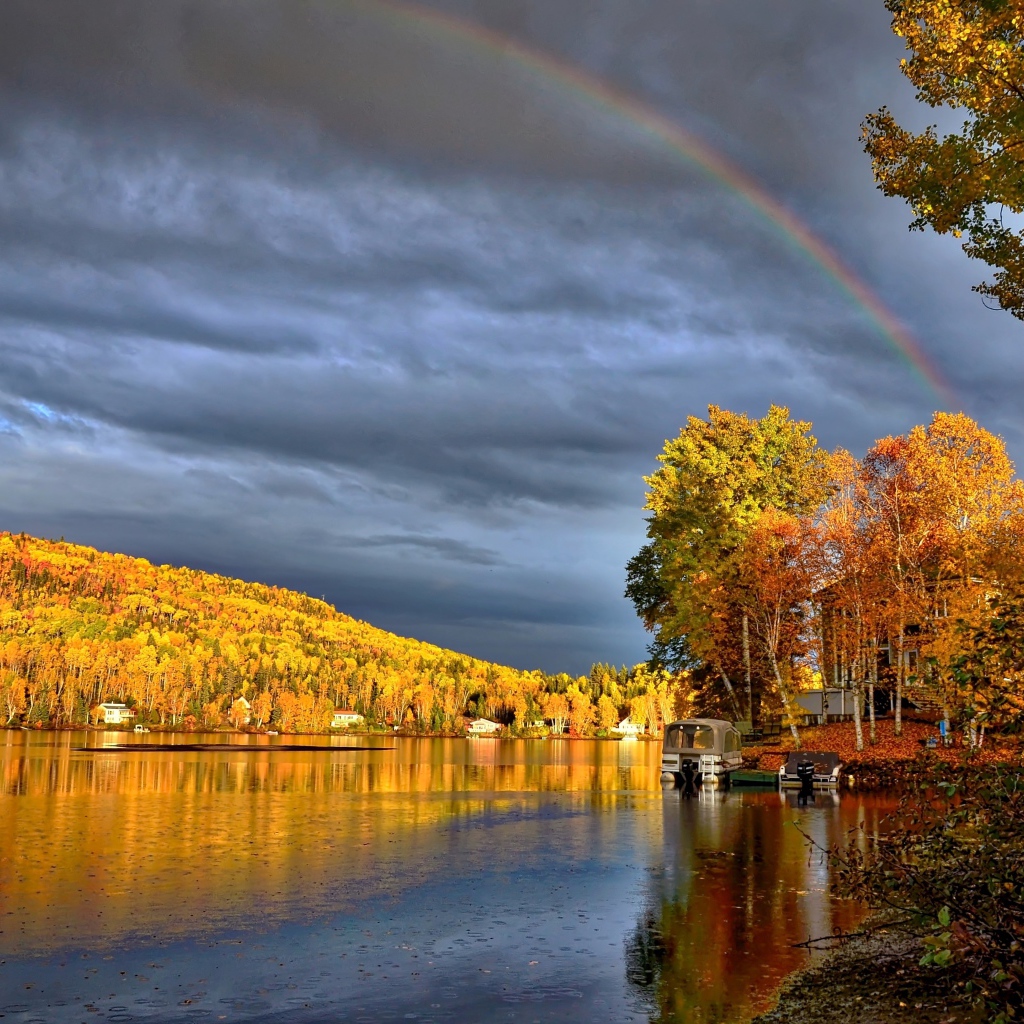 Радуга в пасмурном небе над озером у осеннего леса