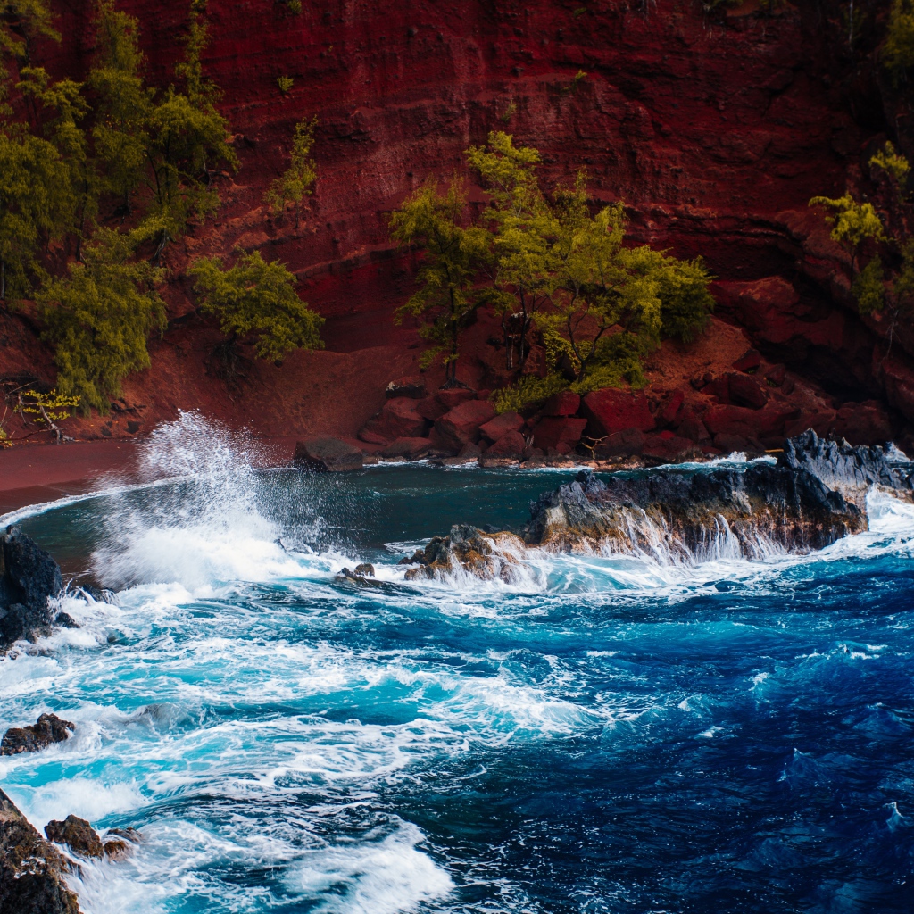 Грубое море брызгает камнями перед красным песчаным океанским заливом в Хане